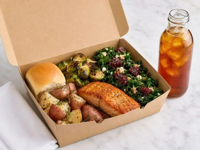 Winslow’s Catering Redwood City office meal box filled with salmon, charred sprouts, composed kale salad, rustic potatoes, and bottled iced tea.